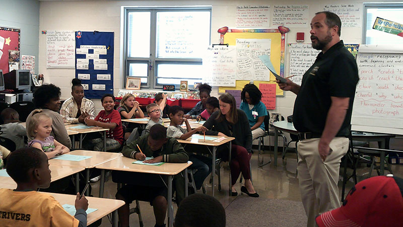 Mr. Seidel, a third grade teacher at Jefferson, stands and reads to his class along with family members in the classroom.