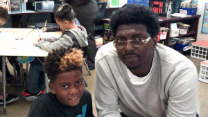 A third grade student and his guest sit in the classroom during family day.