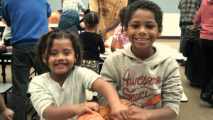Two Students smiling big as they have fun working on their pumpkins.