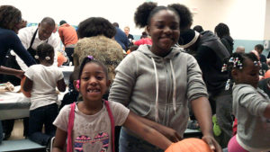 A kindergarten student and her middle school helper take a break from carving their pumpkin to pose for a picture.
