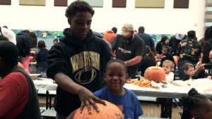 A kindergarten student and his middle school helper take a break from carving their pumpkin to pose for a picture.