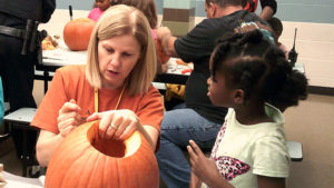 A kindergarten student looks on as Mrs. Teutsch helps design her pumpkin.