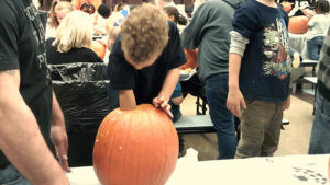 A Kindergarten student works hard to clean out his pumpkin before he and his helper carve it.