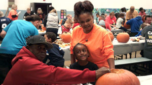 A kindergarten student poses for a picture while he and his family work on carving their pumpkin.