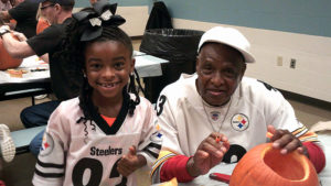 A kindergarten student poses for a picture while she and her helper carve their pumpkin.