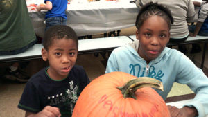 A kindergarten student and his middle school helper pose for a picture while they work on their pumpkin.