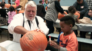 A kindergarten student and her helper working on their pumpkin together.