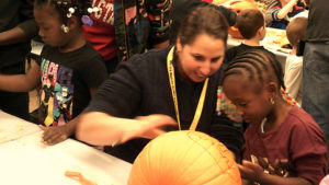 Associate Superintendent Mrs. Hartzell helps a kindergarten student clean out her pumpkin.