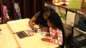 A 1st grade student watches on as her guest helps her complete their family day activity.