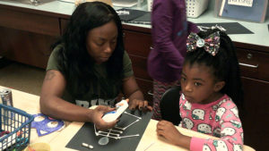 A 1st grade student completes a skeleton craft with the help of her special guest.