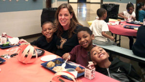 Mrs. Goodyear sits with some first grade students as they enjoy their Thanksgiving meal.