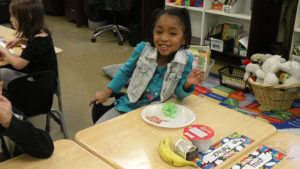 A first grader smiles for the camera as she waits to start her breakfast.