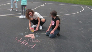 A Harding student and a third grader use the sidewalk chalk to draw on the playground.
