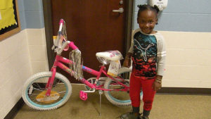 A kindergarten student stands next to her brand new bike.