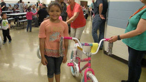 A kindergarten student stands next to her brand new bike.