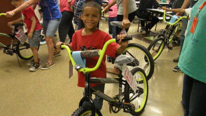 A kindergarten student smiles standing next to his new bike.