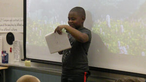 A student reads a poem that he created for the class and guests.