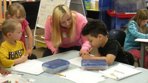 A kindergarten student works on his poetry as his guest looks on.