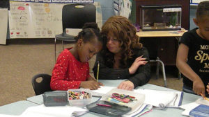 A kindergarten student works on her poetry as her teacher watches.