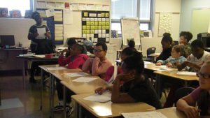 Students sit at their desks while the teacher explains their next activity.