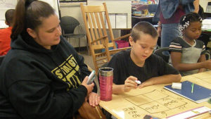 A family member looks on as a student explains his work.