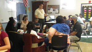 Students and family members listen as their activity is explained to them.