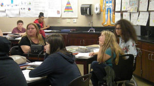Families and students listen as the teacher explains an assignment.