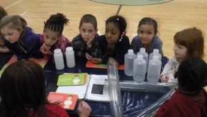 Students listen to the volunteer explain their experiment.