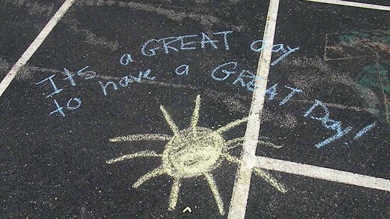 Sidewalk chalk saying "It's a great day to have a great day".