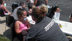 A student gets her face painted as she enjoys a snow cone.