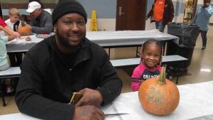 A student and her helper smile before they begin carving their pumpkin.