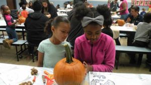 A student and her helper decide what face to put on their pumpkin.