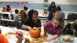 A student cleans out her pumpkin as her helper starts to carve it.