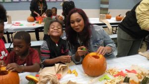 A student and his helper smile as they begin to carve the face of the pumpkin.