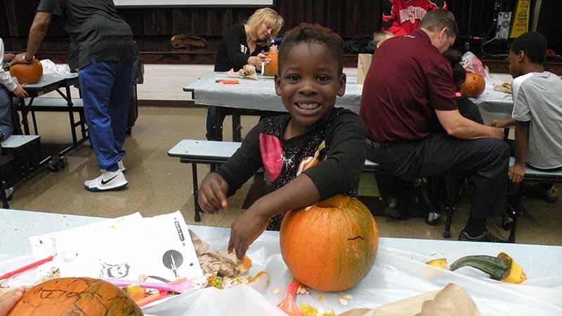 A student smiles as he cleans out his pumpkin.