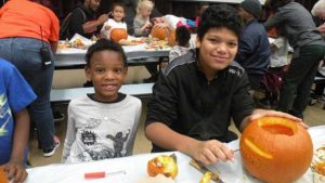 A student and his helper carve their pumpkin.