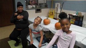 Two students and their helper smile as they wait to carve their pumpkins.