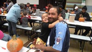 A kindergarten student hugs her helper before they carve their pumpkin.