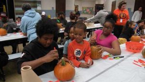 A student watches as his helper begins to carve the pumpkin.