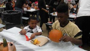 A helper tells the student how to clean out their pumpkin.