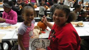 A student and her helper smile as they take a break from carving their pumpkin.