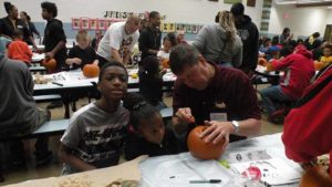 A student watches as their helper carves the pumpkin.