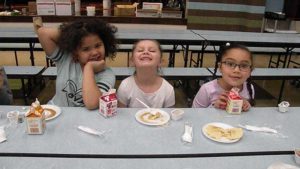 Three first grade students enjoy their pancakes.