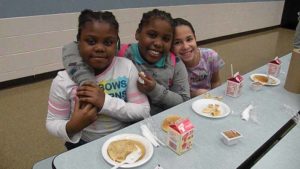 Third grade girls smile for the camera as they enjoy their pancakes.
