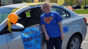 Miss Detate stands next to the car with a poster saying "Sending love from the J".