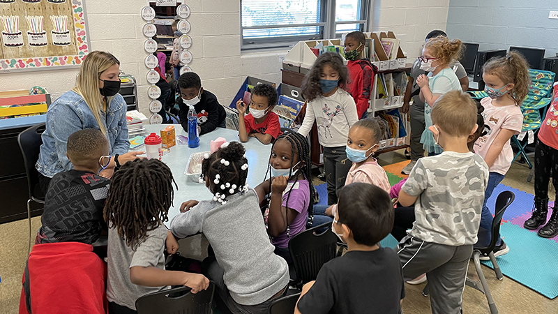 Miss Price's class gathers as she asks questions about their experiment.