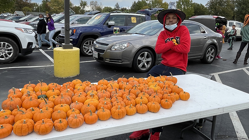 An eighth grade volunteer passes out pumpkins to families.