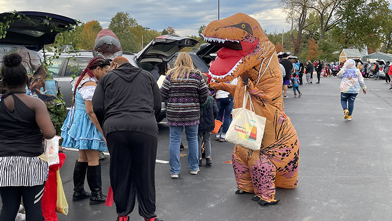 A church member dressed as a dinosaur hands out candy.