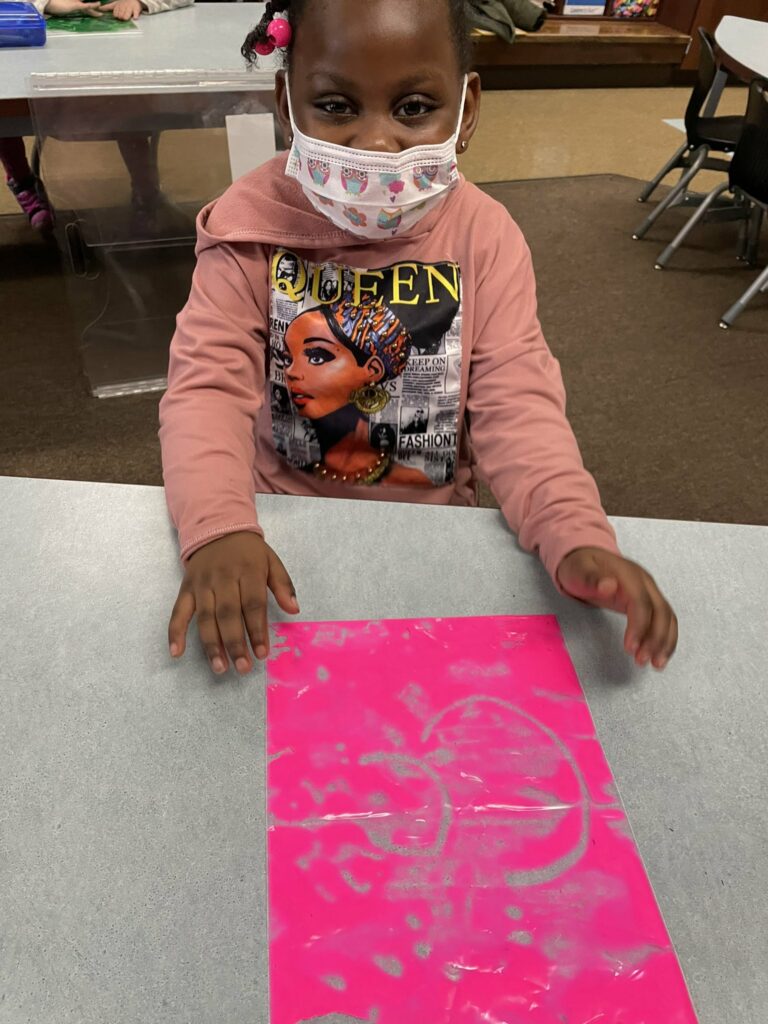 A student uses her paint bag to practice her letters.