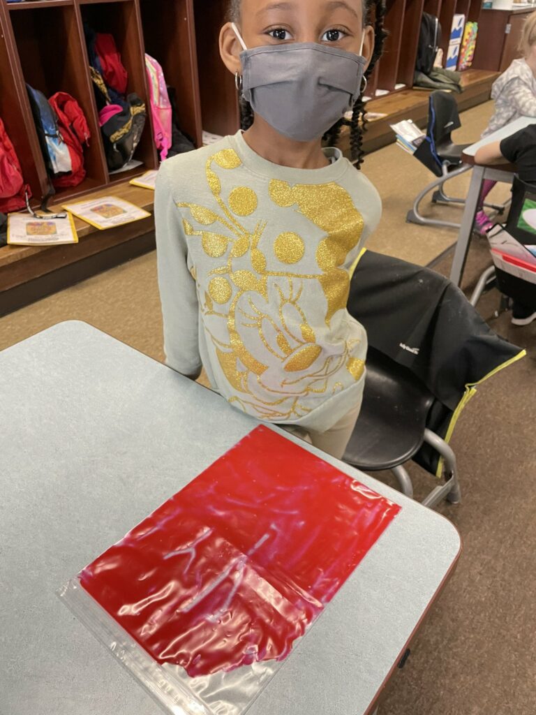 A student uses her paint to practice writing her letters.